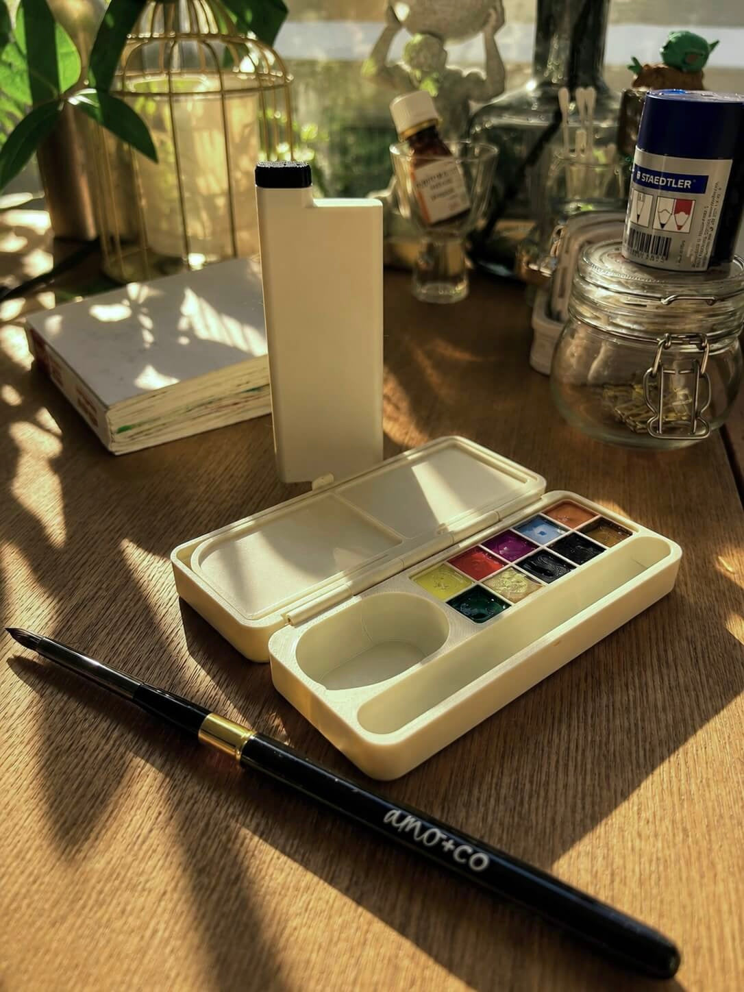 Open amo+co palette with jewel-toned pans and branded brush